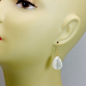 May include: A pair of gold earrings with a white teardrop-shaped gemstone.