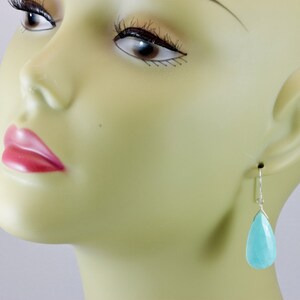 May include: A pair of silver teardrop earrings with light blue gemstone drops.