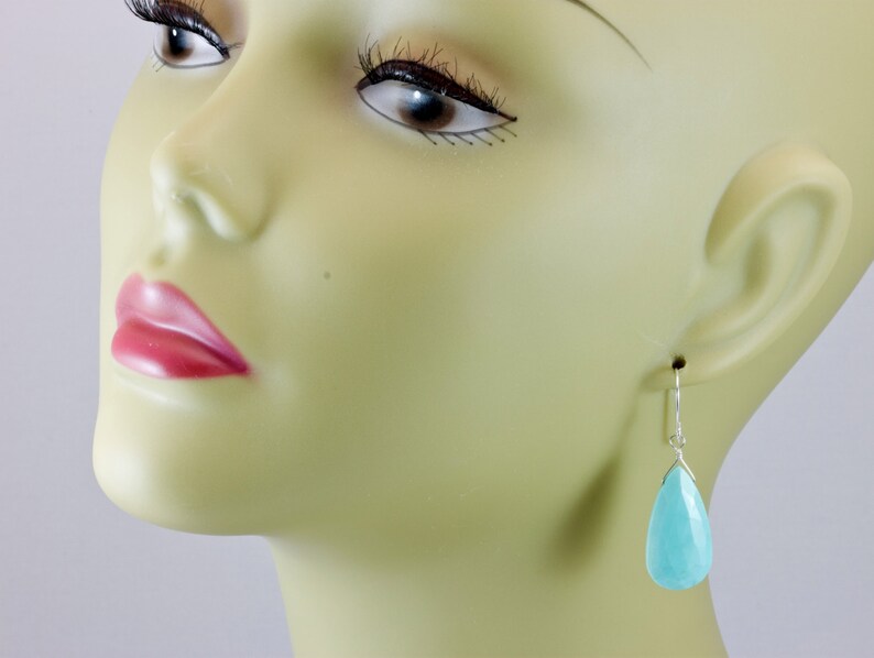 May include: A pair of silver teardrop earrings with light blue gemstone drops.