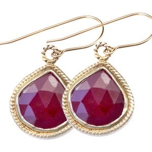 May include: A pair of gold earrings with a teardrop-shaped red gemstone set in a gold bezel. The earrings have a twisted wire design.