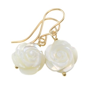 May include: A pair of gold earrings with white mother of pearl rose flower charms. The earrings have a simple hook closure.
