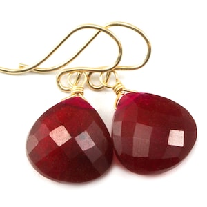 May include: A pair of gold earrings with red gemstone drops. The gemstones are faceted and have a teardrop shape.