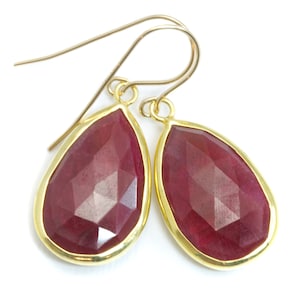 May include: A pair of gold teardrop earrings with red gemstone accents.