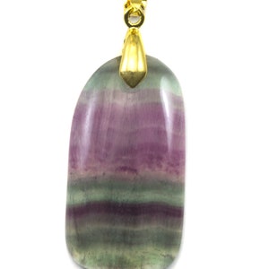 May include: A gold pendant with a green, purple, and pink fluorite stone. The stone is oval shaped and has a smooth, polished finish.