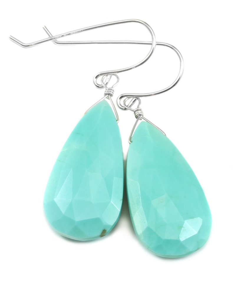 May include: A pair of silver teardrop earrings with turquoise gemstones. The earrings are made with a simple wire design and have a delicate, feminine look.