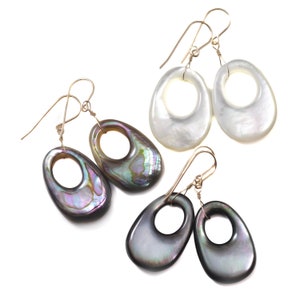 May include: Three pairs of oval-shaped earrings with a hole in the center. The earrings are made of iridescent mother-of-pearl in shades of white, black, and iridescent green. The earrings are attached to gold-colored hooks.