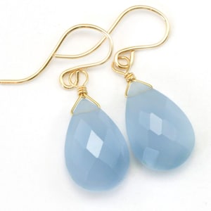 May include: A pair of teardrop-shaped earrings with light blue faceted gemstones and gold-toned wire.