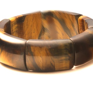 May include: A brown and gold tiger's eye stone bracelet with a polished finish. The bracelet is made of multiple rectangular beads that are connected together.