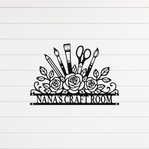 May include: Black metal sign with the text "NANA'S CRAFT ROOM" and decorative elements. The design includes a pencil, paintbrushes, scissors, and roses. The sign is set against a white wood-paneled background.