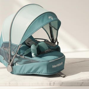 Peut inclure: Un porte-bébé bleu sarcelle et blanc avec un pare-soleil. Le porte-bébé est équipé d'un harnais à cinq points et le mot "Mambaby" est imprimé sur le côté. Le porte-bébé est posé sur une surface en marbre blanc.