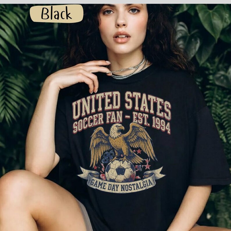 May include: Black t-shirt with a graphic featuring an eagle perched on a soccer ball, the text "UNITED STATES SOCCER FAN - EST. 1994", and "GAME DAY NOSTALGIA". The shirt has a vintage, distressed design.