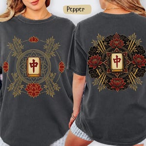 May include: Dark grey t-shirt with a front and back design. The front features a gold and red graphic with bamboo, lotus flowers, and a central tile. The back design is similar.