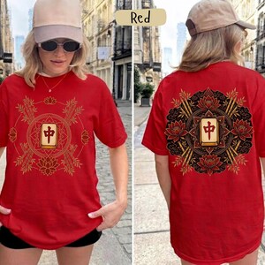May include: Red t-shirt with a gold and black Mahjong tile design on the front and back. The design includes lotus flowers, bamboo stalks, and a central tile. The shirt is a short-sleeved, casual style.