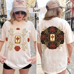 May include: Ivory t-shirt with front and back designs. The front features a central rectangular graphic with Chinese characters, encircled by bamboo, lotus flowers, and a circular border. The back design mirrors the front, with a similar arrangement of elements.