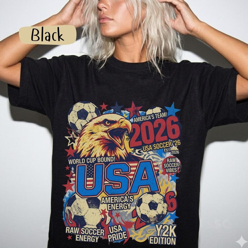 K&ouml;nnte beinhalten: Schwarzes T-Shirt mit einem Grafikdesign, das einen Adler, Fu&szlig;b&auml;lle und den Text "USA 2026" zeigt. Das Design enth&auml;lt den Text "World Cup Bound!" und "America's Team!" in Rot, Wei&szlig; und Blau.