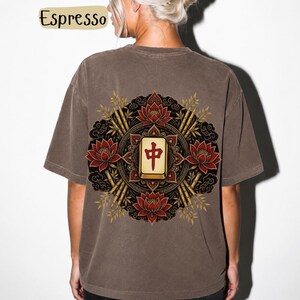 May include: Espresso-coloured t-shirt with a detailed graphic on the back. The design features a central tile with Chinese characters, surrounded by red lotus flowers, bamboo stalks, and ornate black and gold accents. The shirt has a relaxed fit.