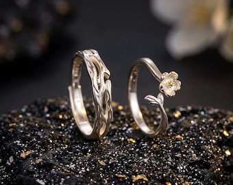 May include: Two silver rings featuring nature-inspired designs. One ring has a textured, branch-like pattern with open cutouts. The second ring is a delicate band topped with a small, five-petaled flower with a gold-toned center and a single leaf.