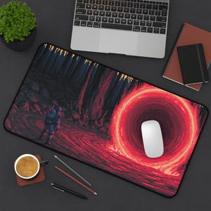 Könnte beinhalten: Rechteckige Schreibtischunterlage mit einer pixeligen Illustration einer Figur in einer dunklen Landschaft mit einem roten Portal. Eine weiße Computermaus liegt auf der Unterlage, zusammen mit einem Laptop, Notizbüchern und einer Kaffeetasse.