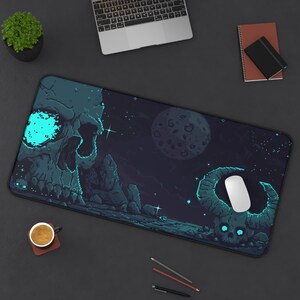 Könnte beinhalten: Eine rechteckige Schreibtischunterlage mit einer Pixel-Art-Landschaft, die einen großen Schädel auf der linken Seite und einen gehörnten Schädel auf der rechten Seite zeigt, vor einem dunklen Sternenhimmel mit Mond. Das Design nutzt Blau- und Schwarztöne.