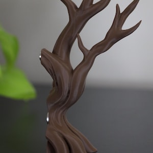 May include: A brown, tree-shaped decorative object. The sculpture has a textured surface and a stylized design with multiple branches. The base is curved and the overall shape is reminiscent of a small tree. The object is likely a decorative item.