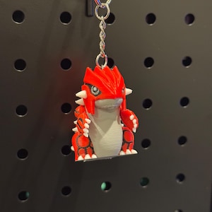 May include: A red and gray 3D-printed keychain featuring a stylized creature with white accents. The keychain is attached to a silver metal ring and chain. The creature has a detailed design with spikes and a distinctive head shape.