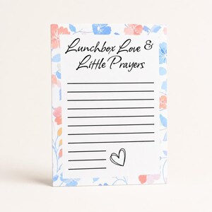 May include: A rectangular notepad with a floral border in shades of pink and blue. The notepad has lined pages and the text "Lunchbox Love & Little Prayers" in black script. A small heart is drawn at the bottom.