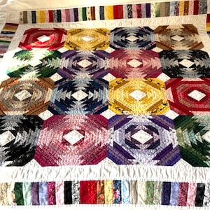 Può includere: Una trapunta fatta a mano con motivo ad ananas composta da una griglia di dodici blocchi ottagonali in vari colori, tra cui rosso, giallo, blu, viola e verde. Ogni blocco presenta un centro a forma di diamante bianco e un bordo multicolore.