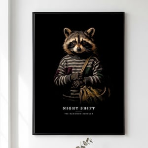 May include: A framed wall art print featuring a raccoon wearing a grey and white striped sweater with a brown shoulder bag. The raccoon is centered against a black background. Below the raccoon, the text reads NIGHT SHIFT THE RACCOON BURGLAR.