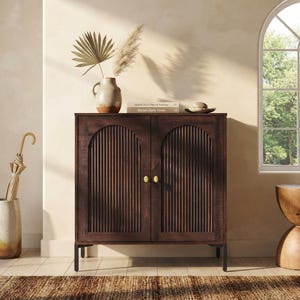 May include: A dark brown wooden cabinet featuring two doors with vertical fluted detailing and small gold knobs. The cabinet stands on four thin black metal legs and has a rectangular frame with arched top panels on each door front.