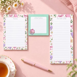 May include: Three stationery pads featuring a white notes pad, a square mint green little notes pad with a book illustration, and a white to-do list pad. All pads are decorated with a repeating pattern of pink bows, daisies, and small books.