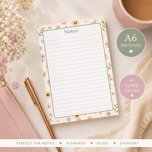 May include: An A6 notepad with 40 lined pages, featuring a cream background decorated with a border of small yellow, pink, and purple flowers and green leaves. The top of the page includes the word Notes: in a dark grey serif font.