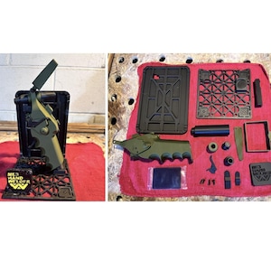 May include: An olive green and black ME3 Hand Welder tool kit featuring a handheld welding device, a black grid base, and various disassembled components including a rectangular frame, small fasteners, and a square plate with the text ME3 HAND WELDER.