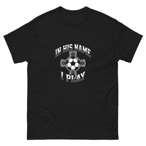 Peut inclure: T-shirt noir avec un graphisme blanc d'un ballon de football à l'intérieur d'une croix, avec le texte "IN HIS NAME I PLAY". Le t-shirt est fait d'une matière douce et confortable.