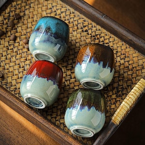 Può includere: Quattro tazze in ceramica dalla forma arrotondata con finitura a smalto reattivo. Ogni tazza presenta un design bicolore con una base color crema chiaro che sfuma in una sezione superiore lucida e scura nei toni del blu, rosso, marrone e verde.