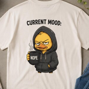 Può includere: T-shirt color crema con la scritta "CURRENT MOOD:" e un'anatra dei cartoni animati con una felpa con cappuccio e una tazza con la scritta "NOPE". L'immagine include anche un berretto da baseball verde, occhiali da sole, scarpe da ginnastica bianche e jeans blu.