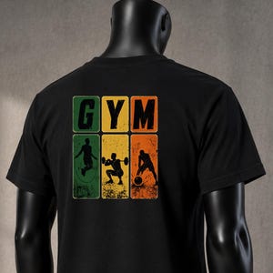 Könnte beinhalten: Ein schwarzes Kurzarm-T-Shirt mit einer Grafik auf der Rückseite und dem Text GYM. Das Design besteht aus drei vertikalen rechteckigen Feldern in Grün, Gelb und Orange, die jeweils die schwarze Silhouette einer trainierenden Person zeigen.