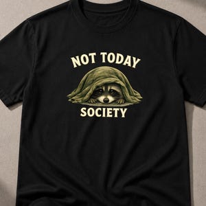 Peut inclure: Un t-shirt noir à manches courtes avec un motif représentant un raton laveur caché sous une couverture verte. Au-dessus du raton laveur, le texte NOT TODAY est écrit en lettres crème, et en dessous, le texte SOCIETY est écrit en couleur crème.