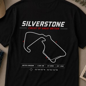 Könnte beinhalten: Schwarzes T-Shirt mit weißer Silverstone-Rennstreckenkarte. Text: "SILVERSTONE CIRCUIT OF GREAT BRITAIN". Enthält Streckendetails: 5,891 km, 18 Kurven, gegründet 1948. Koordinaten sind ebenfalls angegeben.