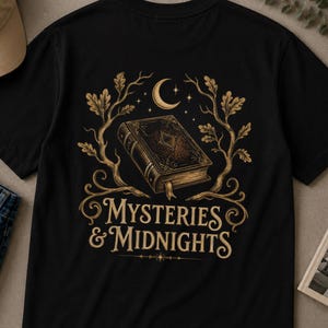 Może przedstawiać: Czarna koszulka z szczegółową ilustracją starej książki, półksiężyca i gwiazd. Projekt zawiera napis "Mysteries & Midnights" w eleganckiej czcionce, z dekoracyjnymi gałęziami. Stylowa koszulka dla miłośników książek.