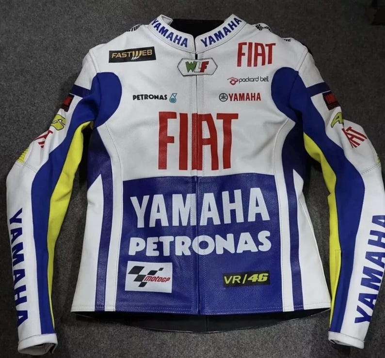 May include: A white, blue, and yellow motorcycle racing jacket featuring prominent red FIAT branding, YAMAHA and PETRONAS logos, and the text VR/46. The jacket includes various sponsor patches such as FASTWEB, WLF, and the MotoGP logo on the front.