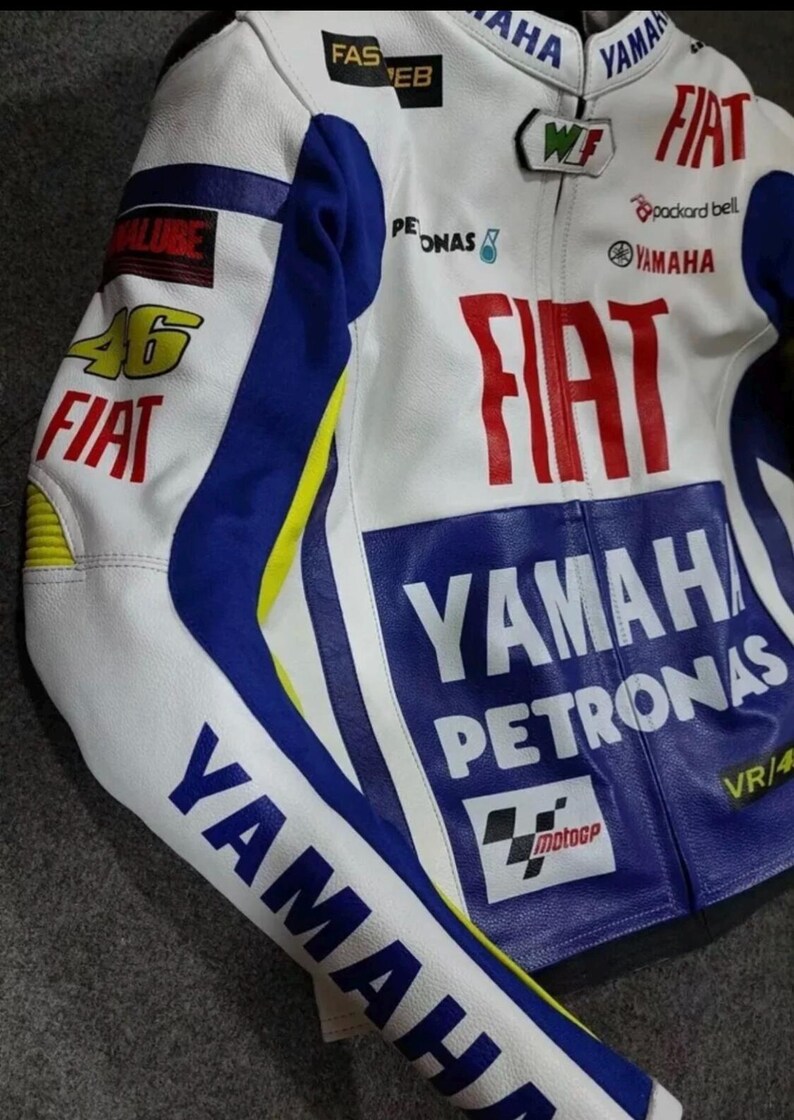 May include: A white, blue, and yellow motorcycle racing jacket featuring prominent branding including Fiat, Yamaha, Petronas, and the number 46. The jacket displays various sponsor logos such as Packard Bell, Fast Web, and the MotoGP emblem on the front.
