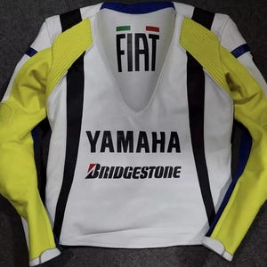 May include: A white, yellow, and black motorcycle jacket featuring the text FIAT with an Italian flag icon at the neckline, YAMAHA in large black letters across the chest, and the Bridgestone logo printed below in black and red lettering.