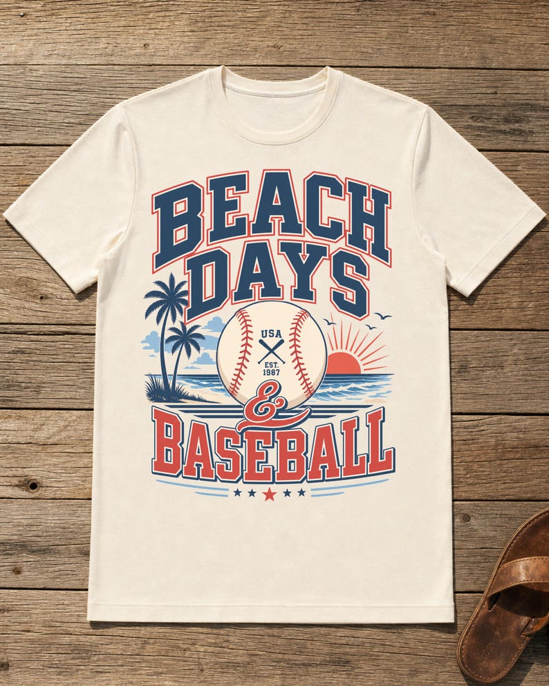 May include: A cream-colored short-sleeve t-shirt featuring a graphic print with the text BEACH DAYS & BASEBALL. The design includes a baseball, palm trees, a sun, and ocean waves in red, blue, and white colors, with USA EST. 1987 on the ball.