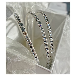 Pode incluir: Três faixas de cabelo brancas com detalhes de strass transparentes. As faixas estão empilhadas.