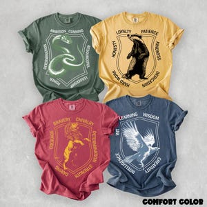 May include: Four short-sleeve t-shirts in olive green, mustard yellow, maroon, and slate blue. Each shirt features a central shield graphic with an animal illustration and surrounding text: snake with AMBITION CUNNING, badger with LOYALTY PATIENCE, lion with BRAVERY CHIVALRY, and eagle with LEARNING WISDOM.