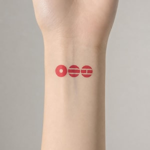 May include: A temporary tattoo on a wrist featuring three red circular icons arranged horizontally. The first circle has a central dot, the second contains two horizontal lines, and the third displays a horizontal line bisecting the circle.