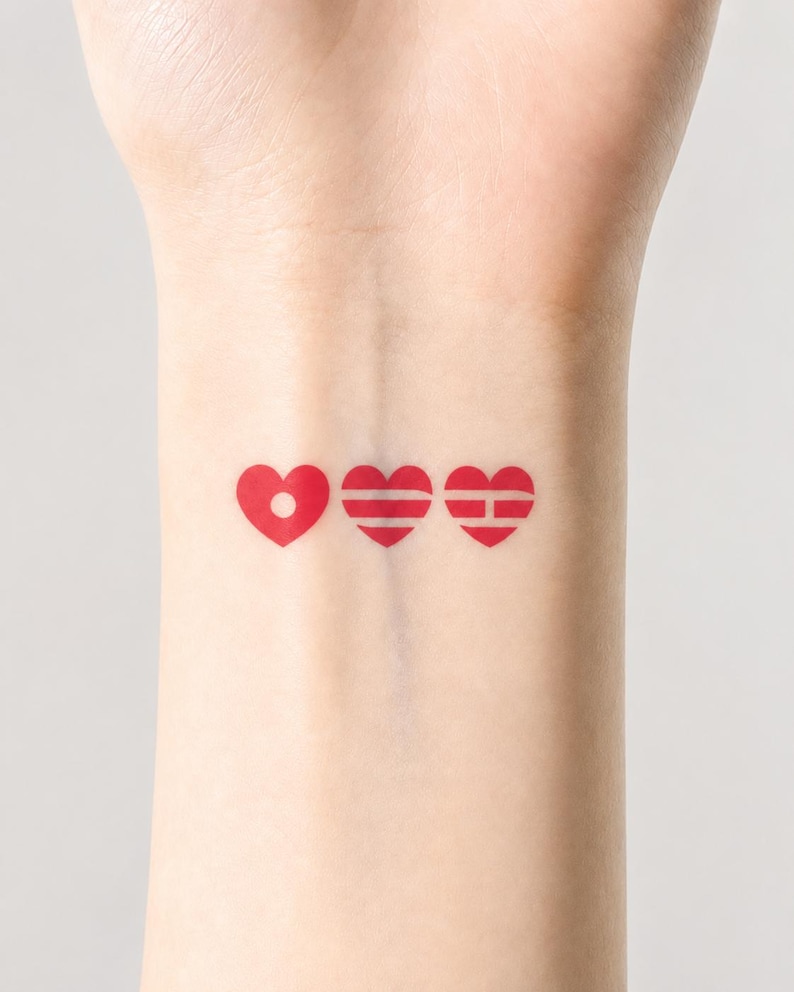 May include: Three red heart temporary tattoos on a wrist. The first heart has a dot in the center, the second has horizontal lines, and the third has a horizontal and vertical line.