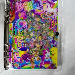 Op de afbeelding: Een doorzichtige map met een kleurrijk Lisa Frank-ontwerp. Het ontwerp bevat een regenboogachtergrond, een eenhoorn, een luipaard, puppy's en het Lisa Frank-logo. De map is gevuld met stickers en heeft een zilveren metalen ringband.