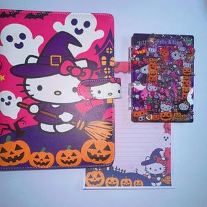 Puede incluir: Un cuaderno rosa con temática de Halloween que muestra a Hello Kitty vestida de bruja con fantasmas y calabazas, un bloc de notas rayado a juego con un gráfico de Hello Kitty bruja y una pequeña carpeta de plástico transparente con confeti.