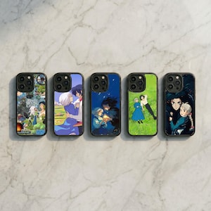 May include: Five black phone cases with colorful anime-style illustrations. The cases feature various scenes and characters, including couples and landscapes. The cases are arranged in a row on a marble surface.